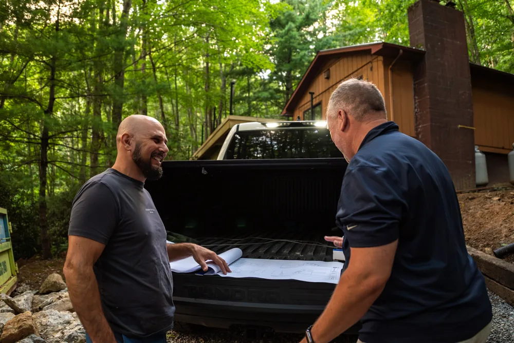 Brad Currin reviewing plans at the truck beside a wooded home site