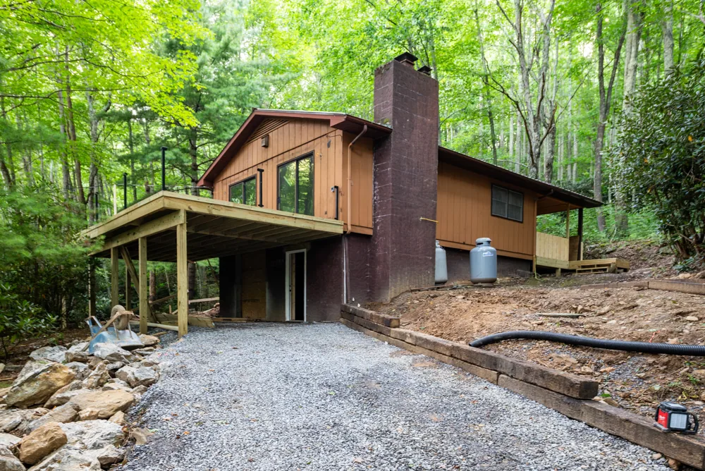 Wood-sided mountain home with a stone chimney, porch and new gravel drive